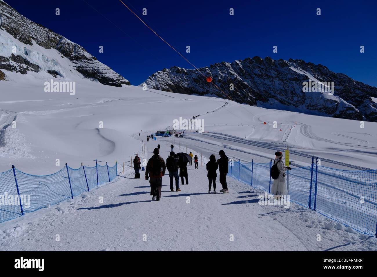 Fieschertal, Switzerland-Oct.2nd 2025: Tourists walking on a snowy path at Jungfraujoch with view of the Alpine mountains Stock Photo