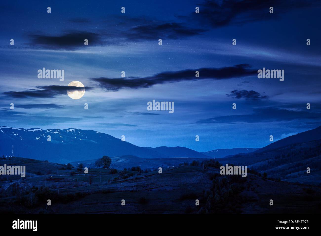 mountainous countryside scenery at night. mysterious sky above the distant valley and ridge. full moon over remote meadows and trees on rolling hills. Stock Photo