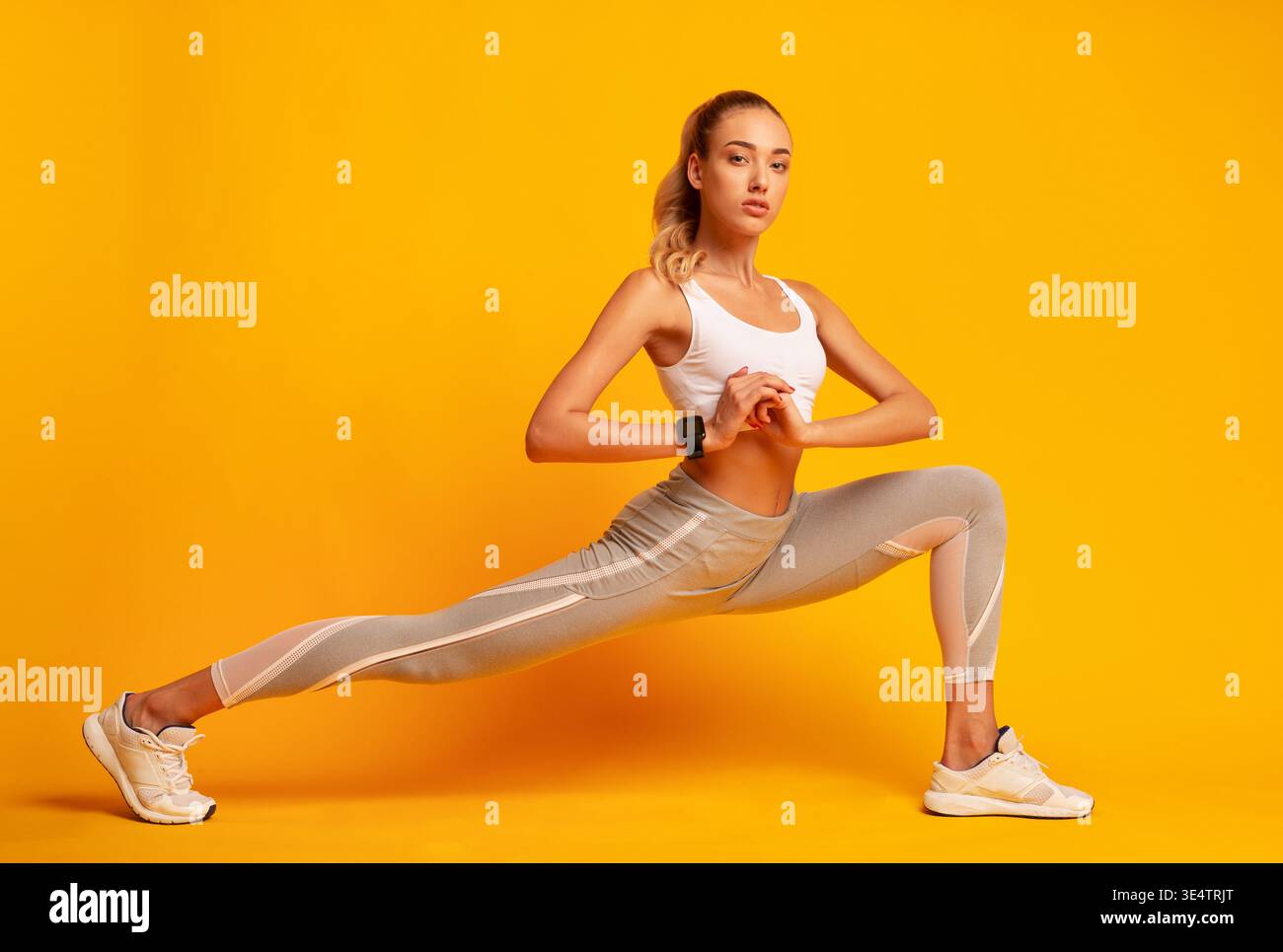 Woman Doing Deep Lunge Exercise Over Yellow Background Stock Photo