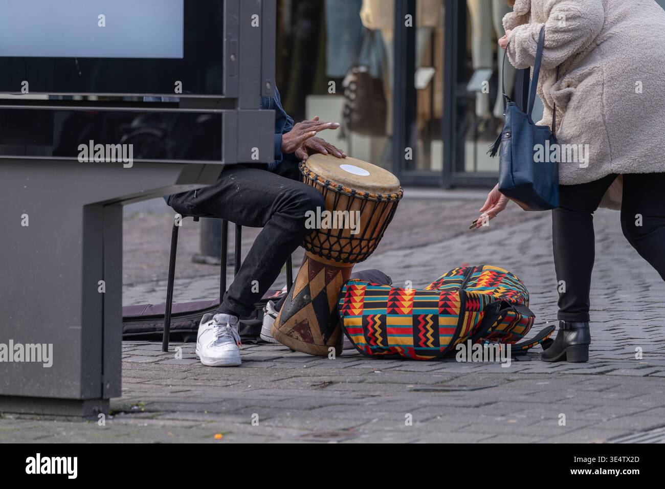 Street musician playing a drum while a passerby gives a donation in an ...