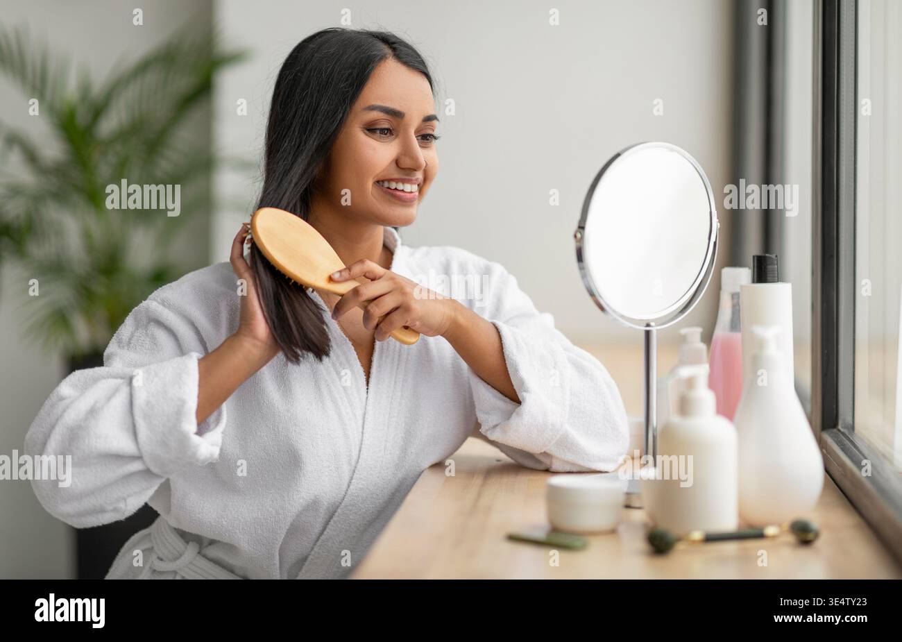 Cheerful indian woman combing beautiful dark long hair at bathroom Stock Photo