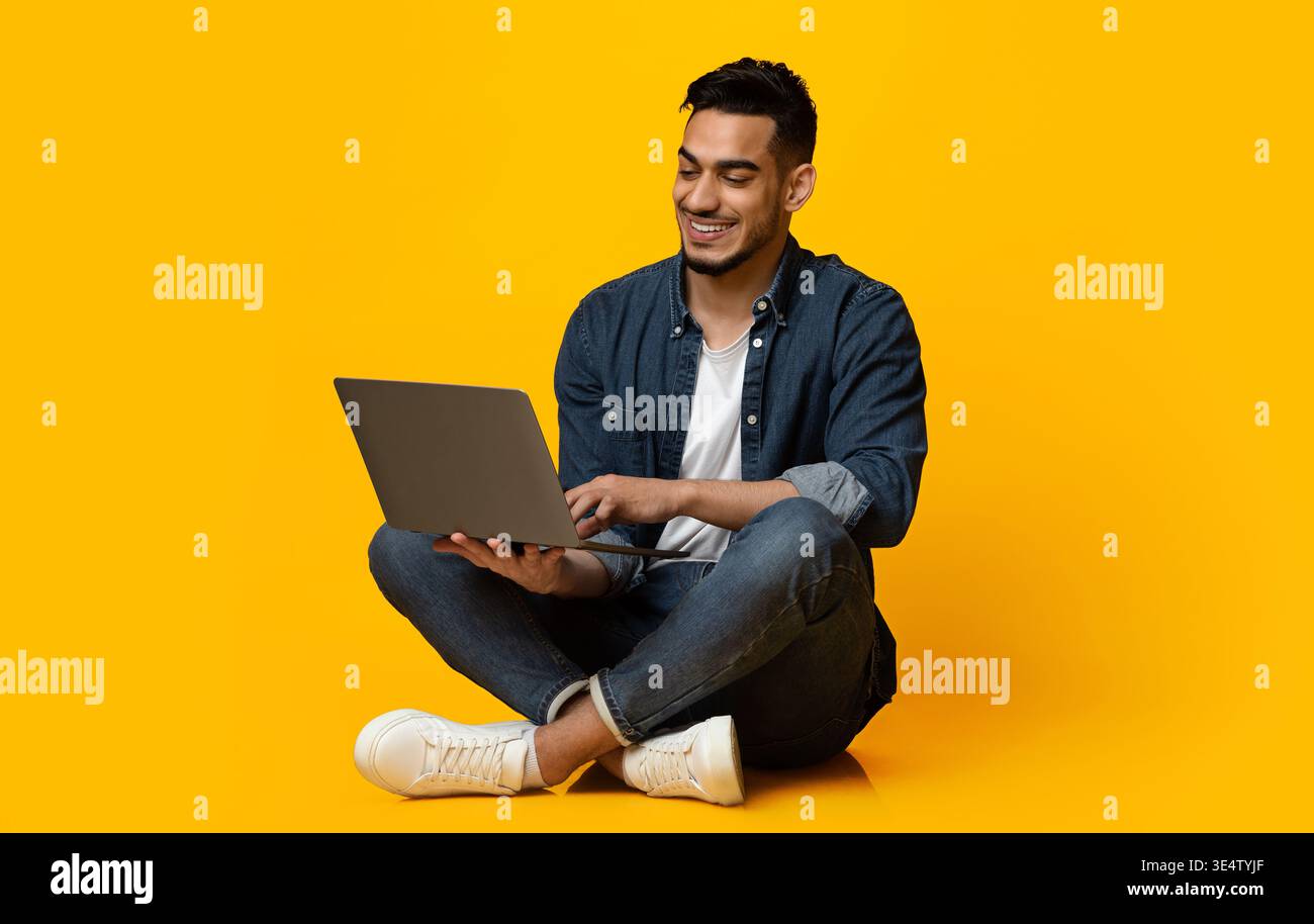 Happy middle eastern guy using modern notebook, isolated on yellow Stock Photo