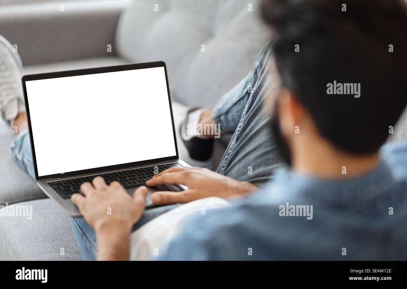 Indian Man Using Laptop Computer With Blank White Screen At Home Stock Photo