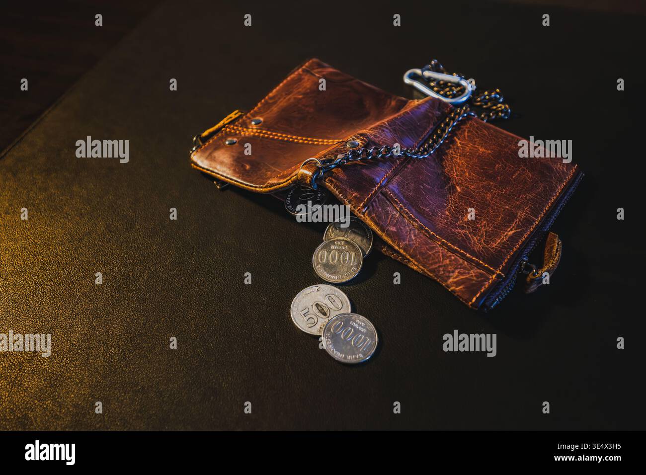 A close-up of a battered, old leather wallet showing only a few low-value Indonesian Rupiah coins left inside. Stock Photo