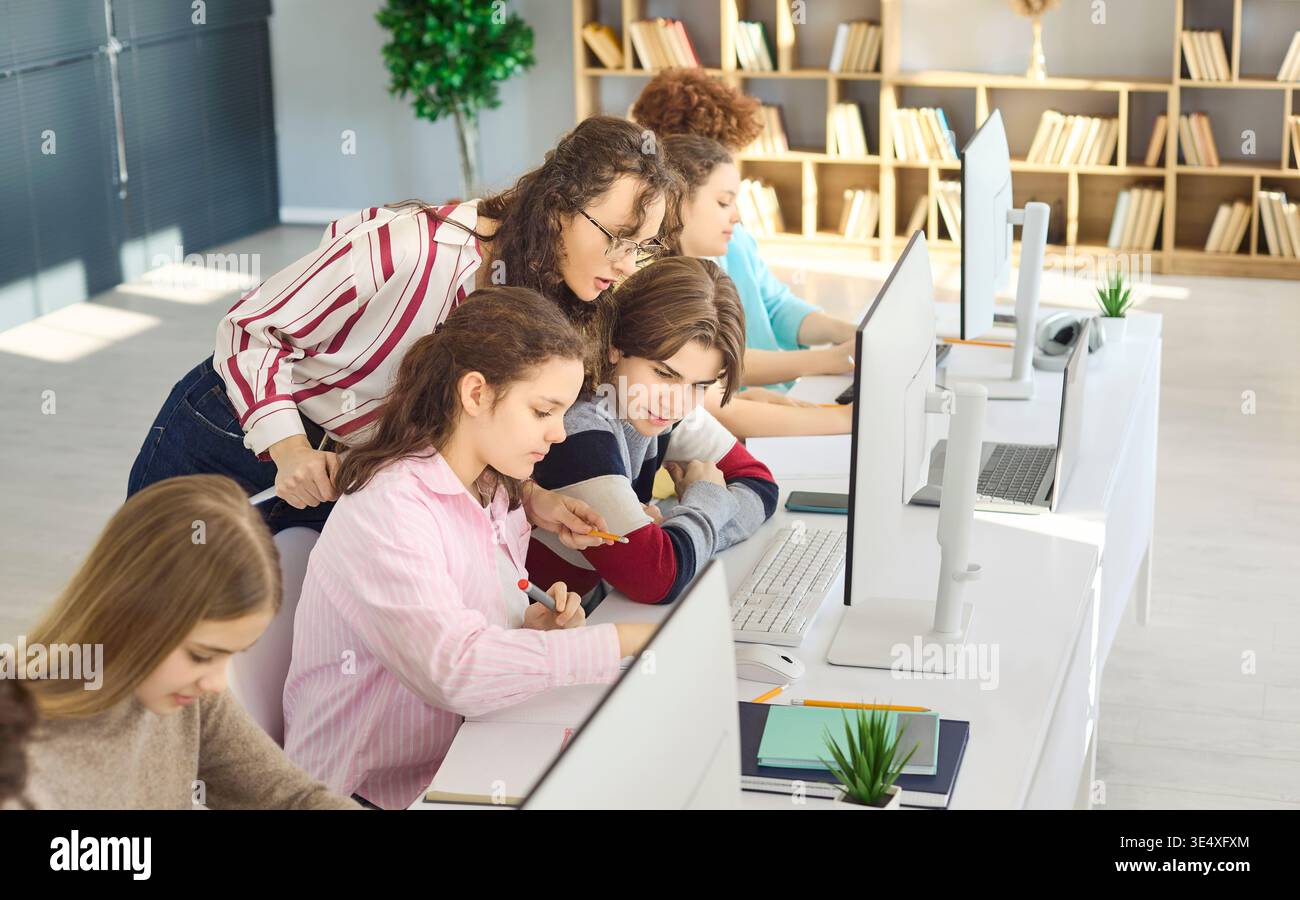 Teacher guiding teen students at computers in classroom lab, collaborative learning Stock Photo