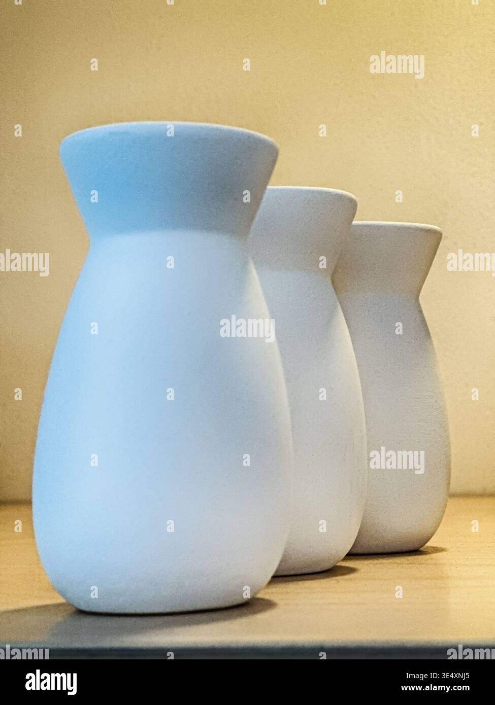 Still life that shows three white ceramic vases against a well-lit background. Stock Photo