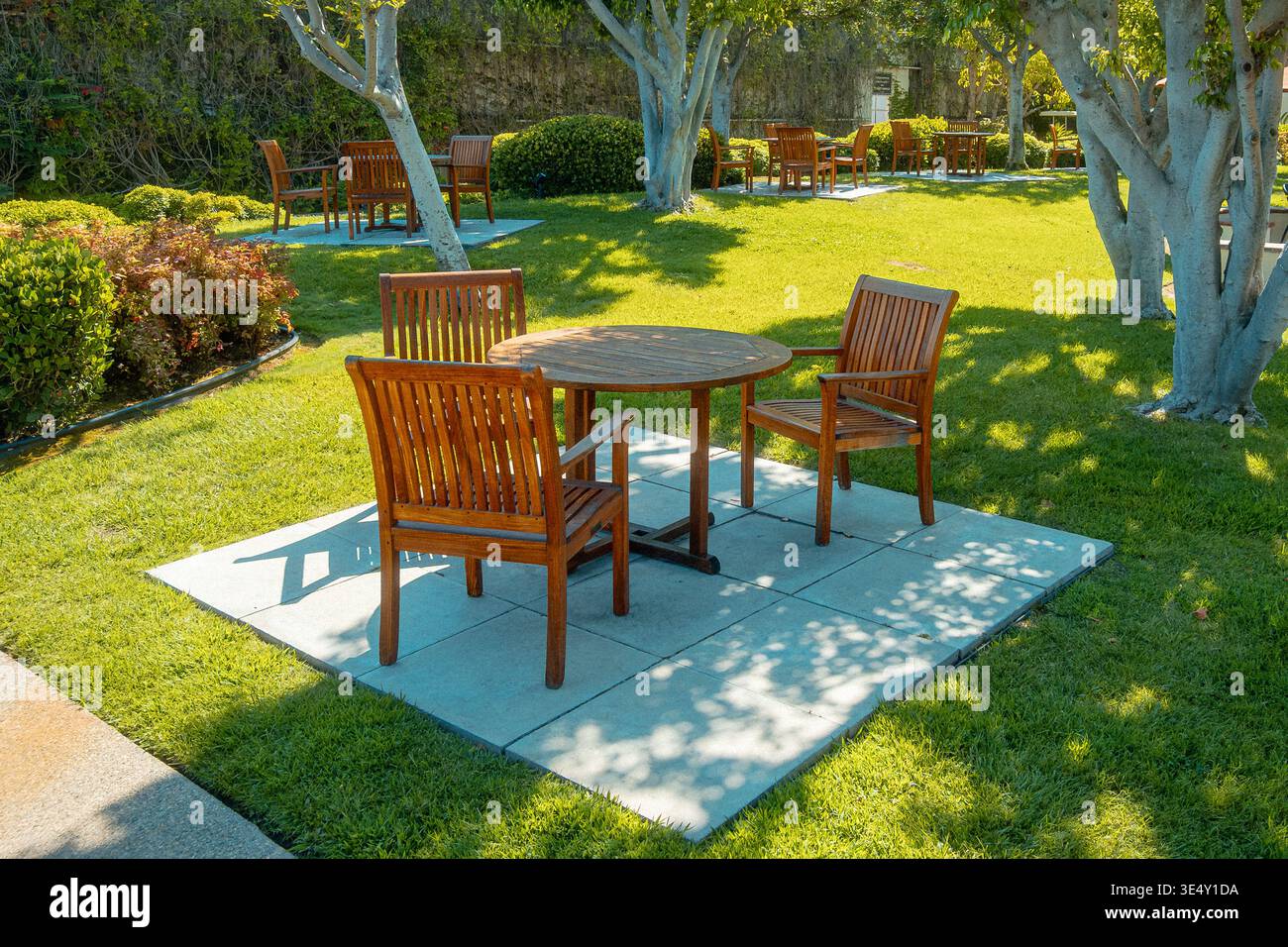 Alfresco Dining Setup. Sunlit Patio With Wooden Furniture. Serene Backyard Scene With Outdoor Table And Chairs Stock Photo
