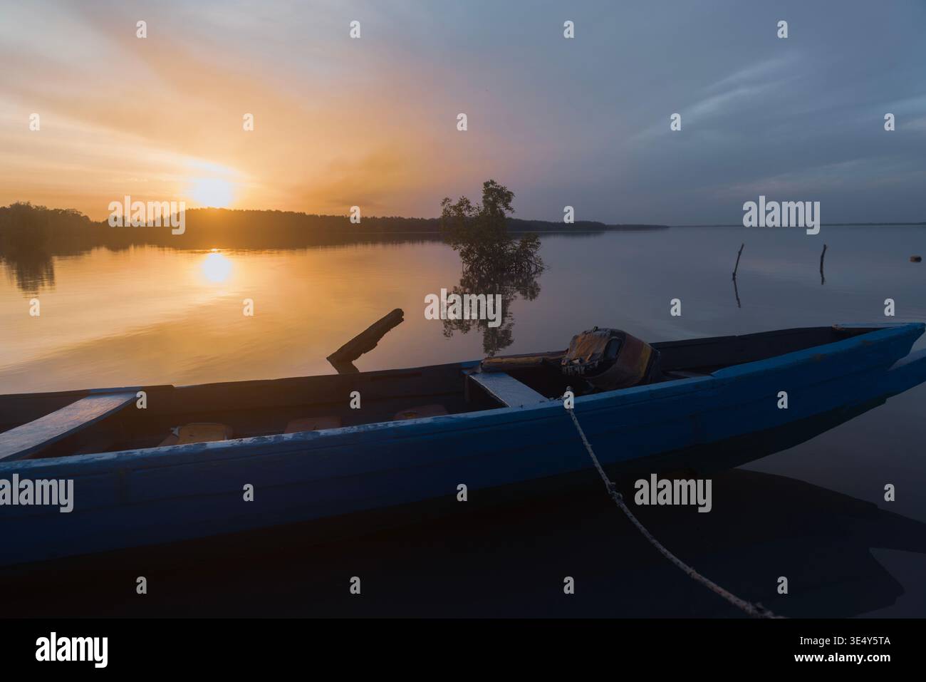 Sunset view of a blue colored wooden canoe at a crumbled jetty in the Gambia river. Tendaba, The Gambia. Stock Photo