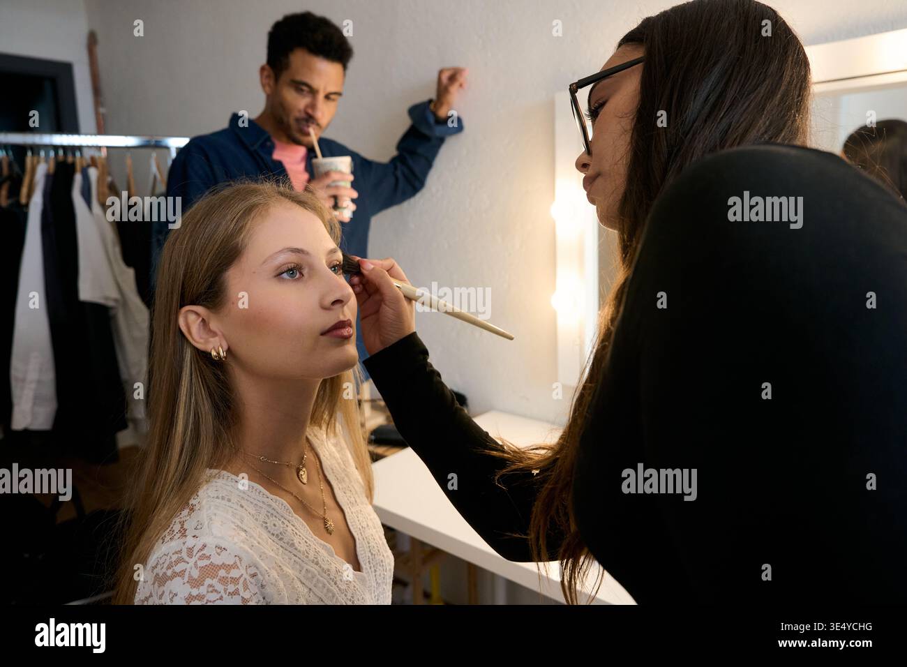 Makeup artist applying cosmetics backstage to young model Stock Photo