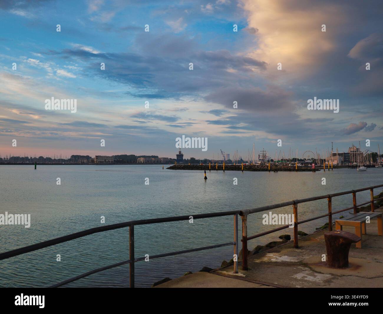 Morgendliche Hafeneinfahrt in Rostock-Warnemünde: Blick von der Pier über die Warnow bei Sonnenaufgang unter einem weiten Wolkenhimmel Stock Photo