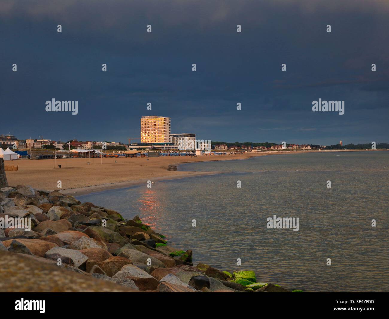 Morgensonne auf dem Hotel Neptun: Das markante Wahrzeichen von Warnemünde leuchtet golden vor einem dunklen Gewitterhimmel am Ostseestrand Stock Photo