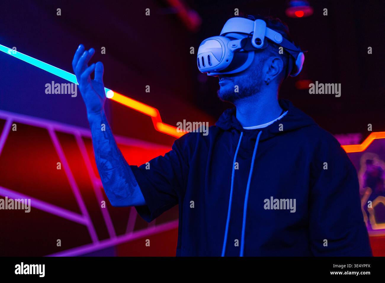Bearded young man in virtual reality glasses in the studio with blue and pink light. Stock Photo