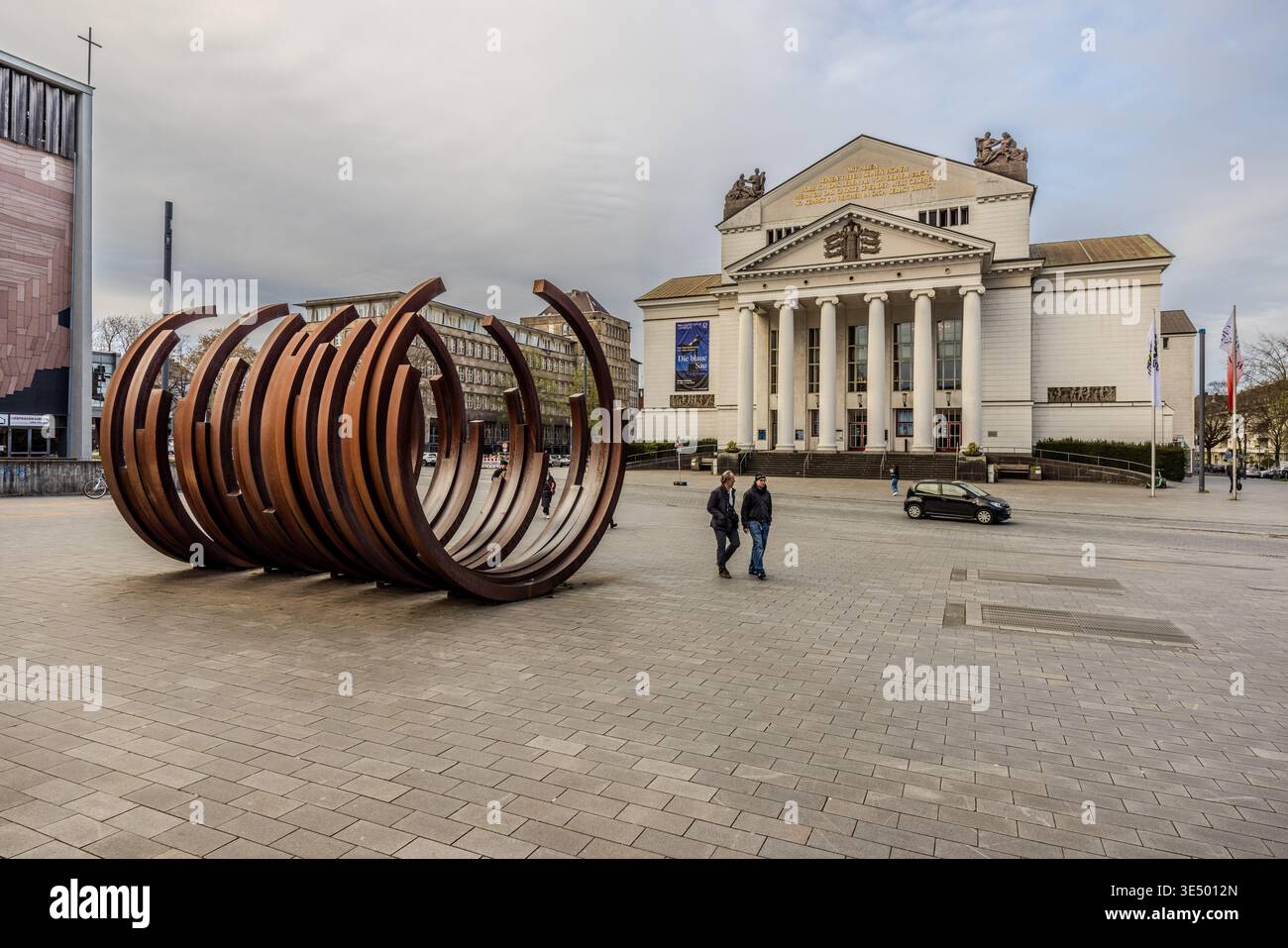 Rheinisches Landestheater (Duisburg Theatre). The sculpture “5 Arcs x 5” by the artist Bernar Venet deliberately references Duisburg’s steel and pig iron era, which shaped the city, whilst its central location symbolises the transition towards culture and modernity. Duisburg, North Rhine-Westphalia, Germany Stock Photo