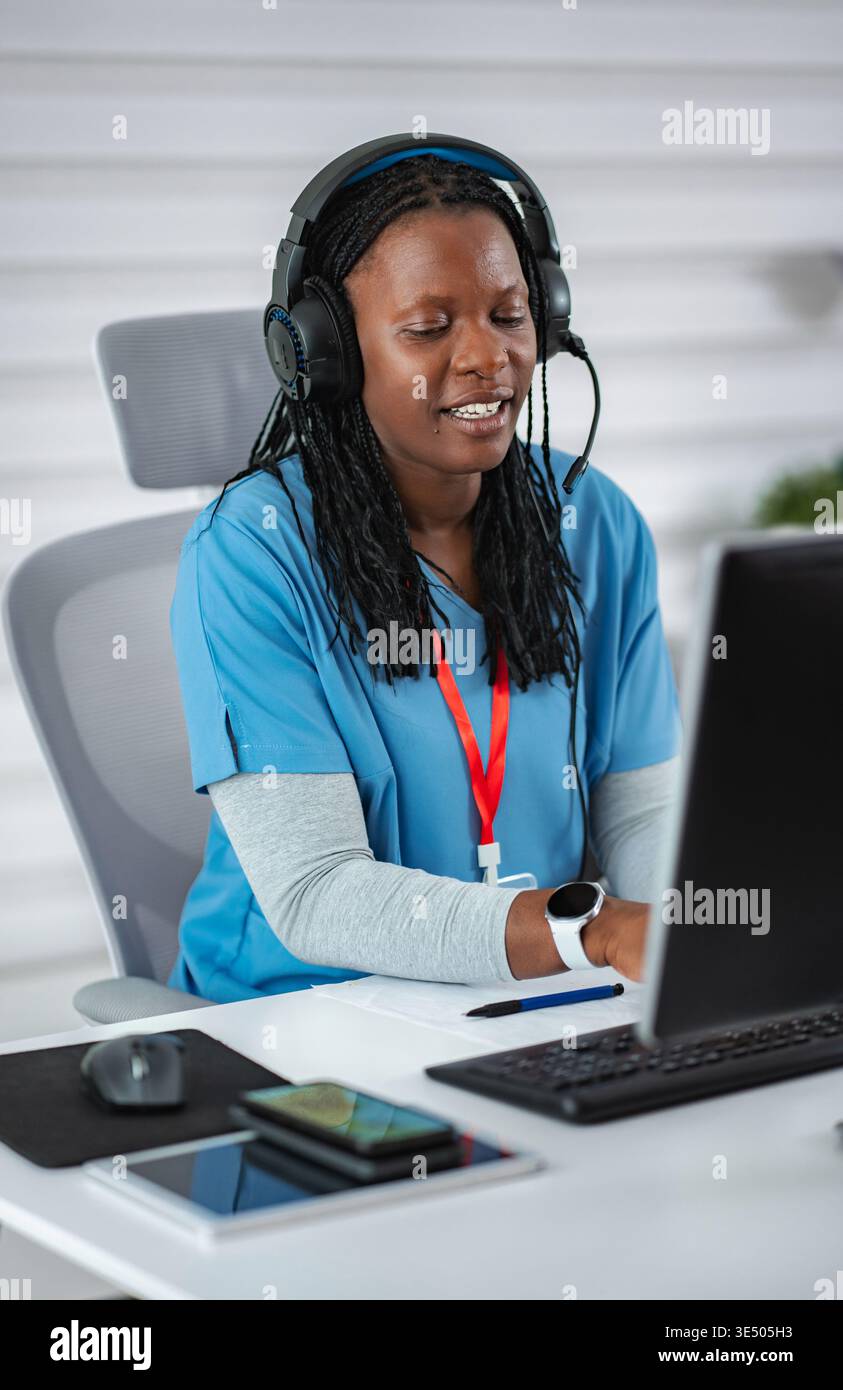 African American woman wearing headset and blue scrubs working on ...