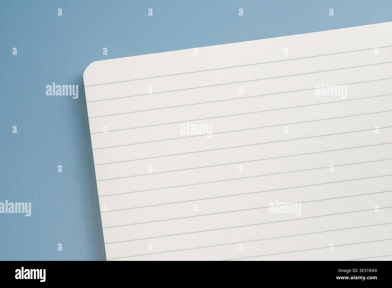 Blank spiral notebook lies open on a blue background. Open pages are lined and ready for writing or drawing. Top view Stock Photo