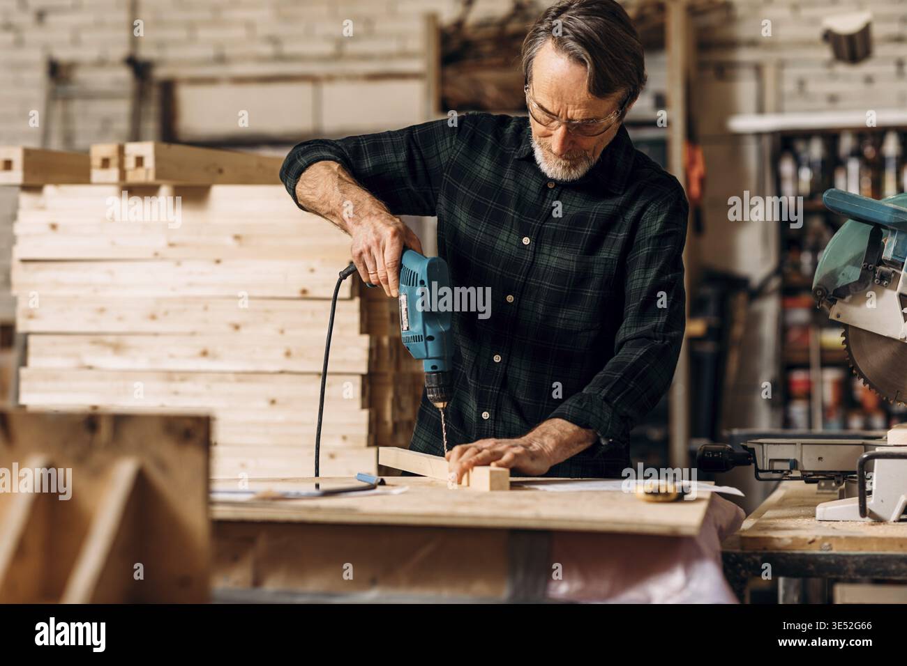 Carpenter using electric drill. Senior man making a hole in a wooden board Stock Photo