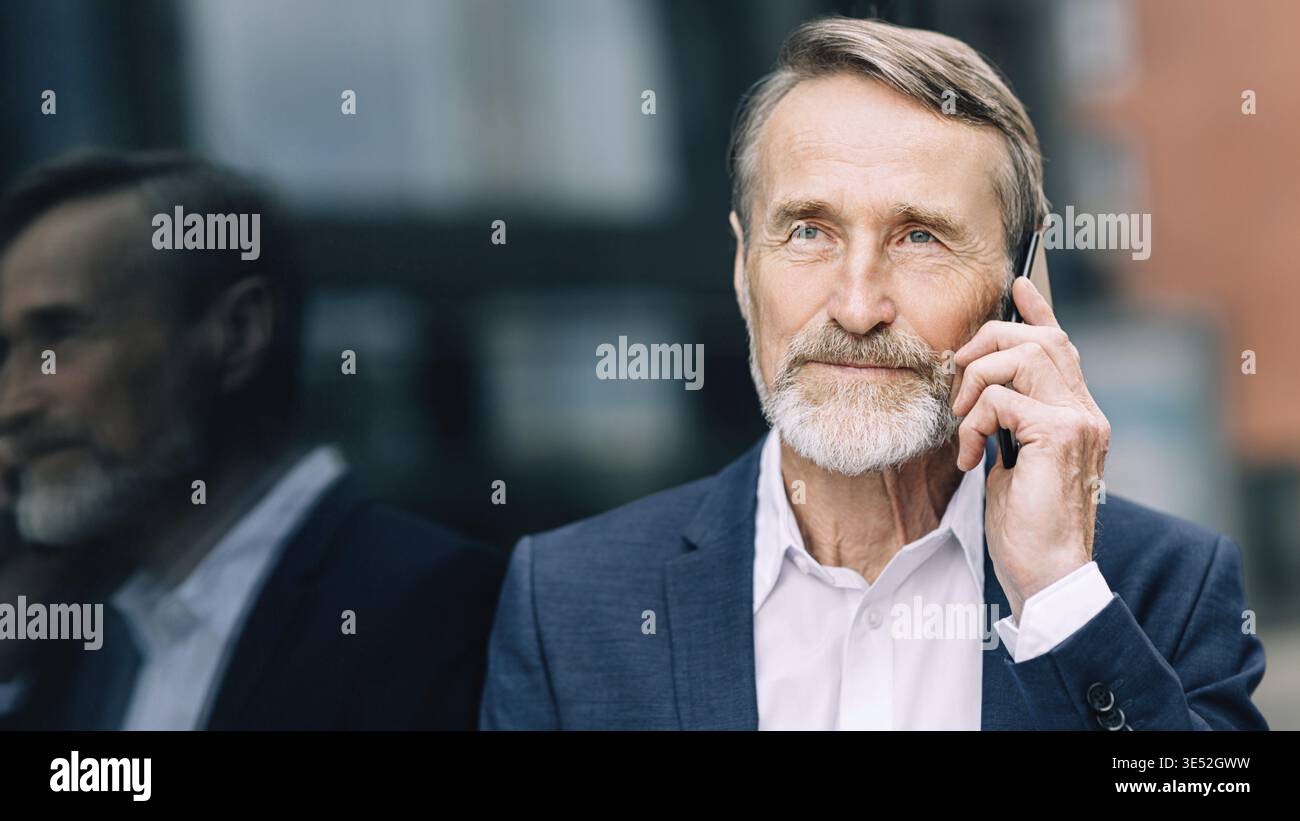 Serious bearded businessman talking on a mobile phone while standing outdoors Stock Photo