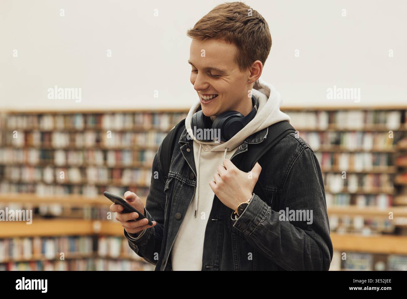 Smiling student using smartphone while standing in library Stock Photo