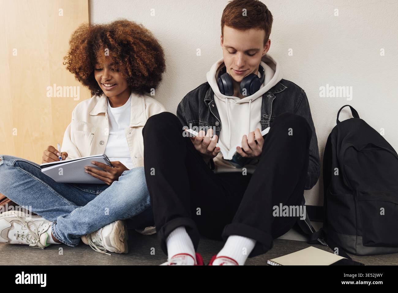 Two classmates sitting at wall in school. Students preparing their assignment while sitting together Stock Photo