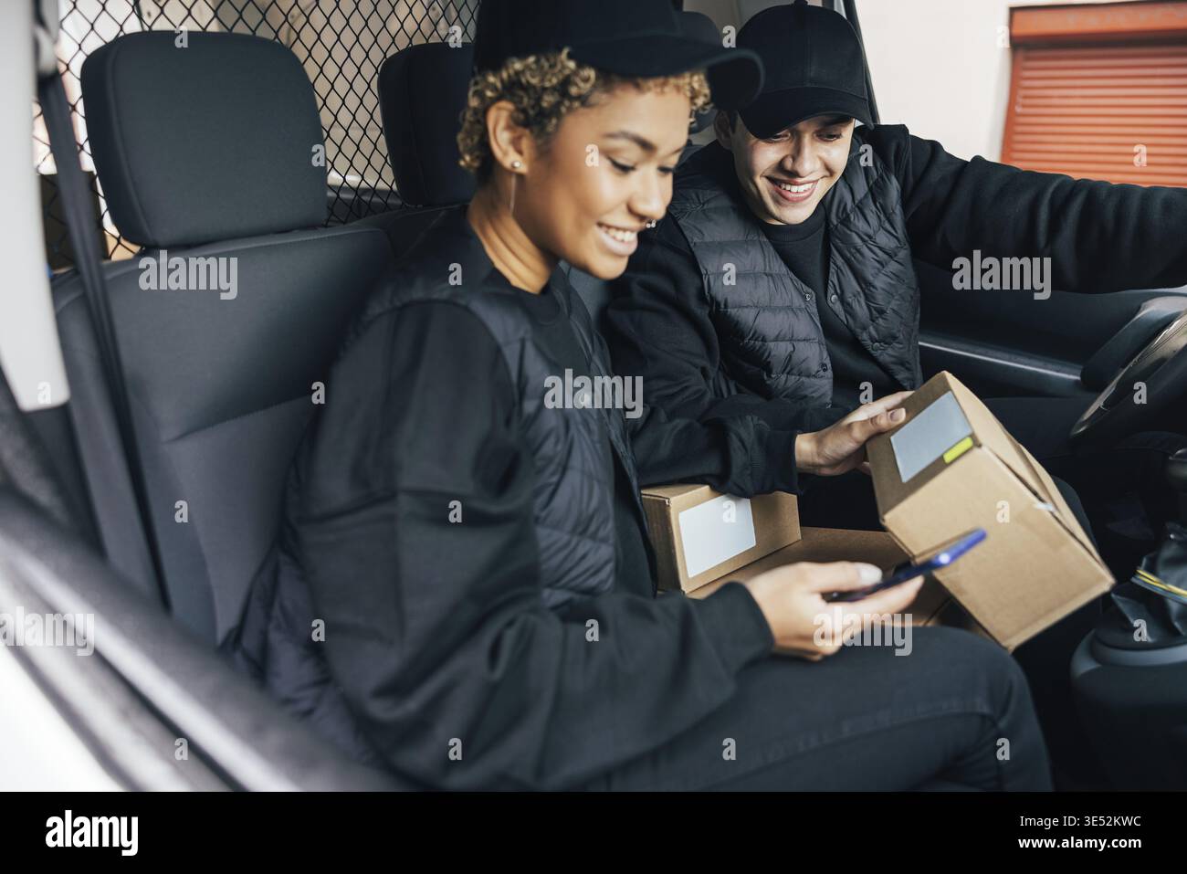 Two couriers sitting in car checking information on box using mobile phone Stock Photo