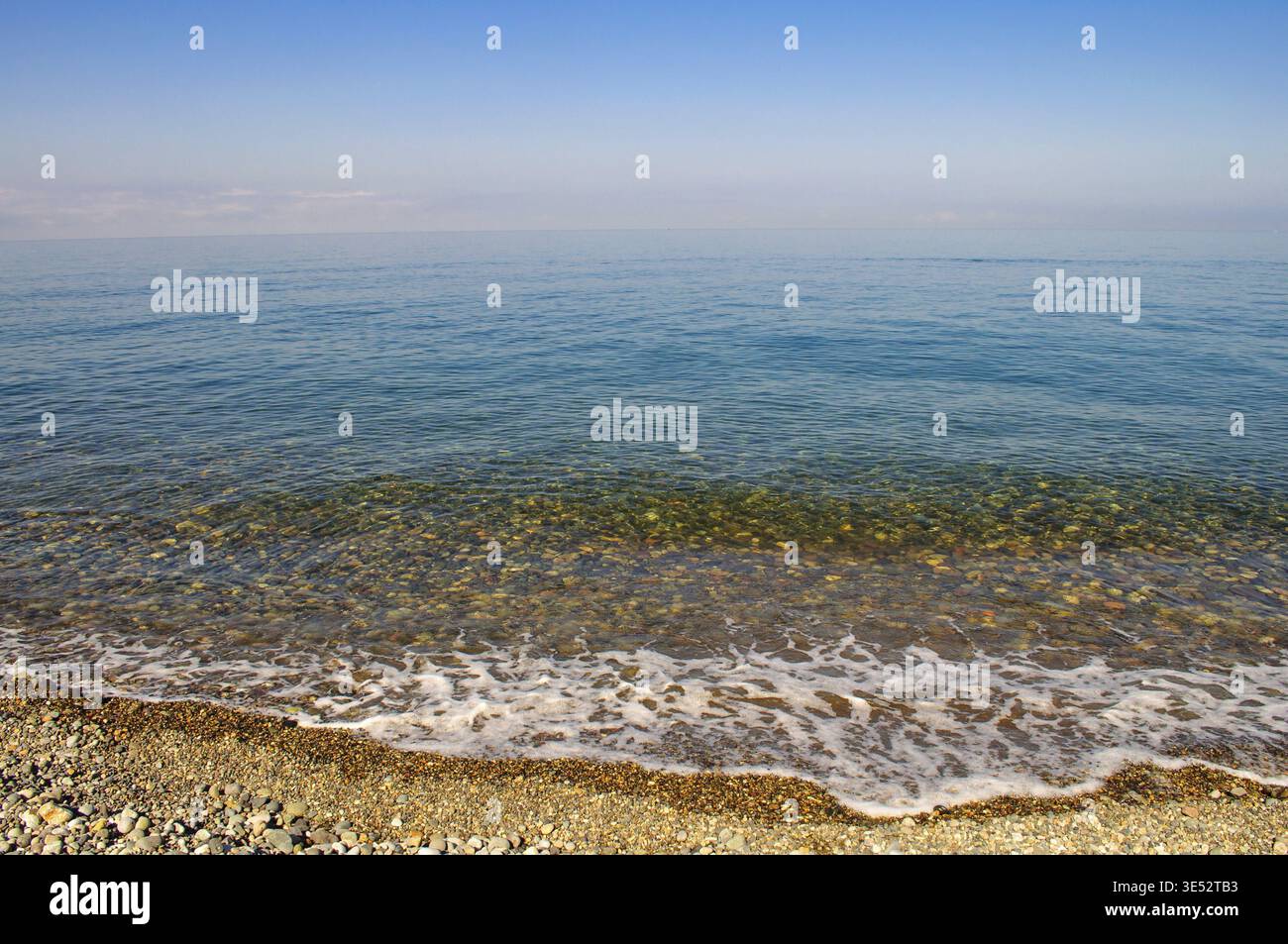 Sommerliche Meereslandschaft mit glattem Wasser und Horizontlinie, klares azurblaues Wasser. Kieselstrand an einem sonnigen Tag, kleine Wellen Stock Photo