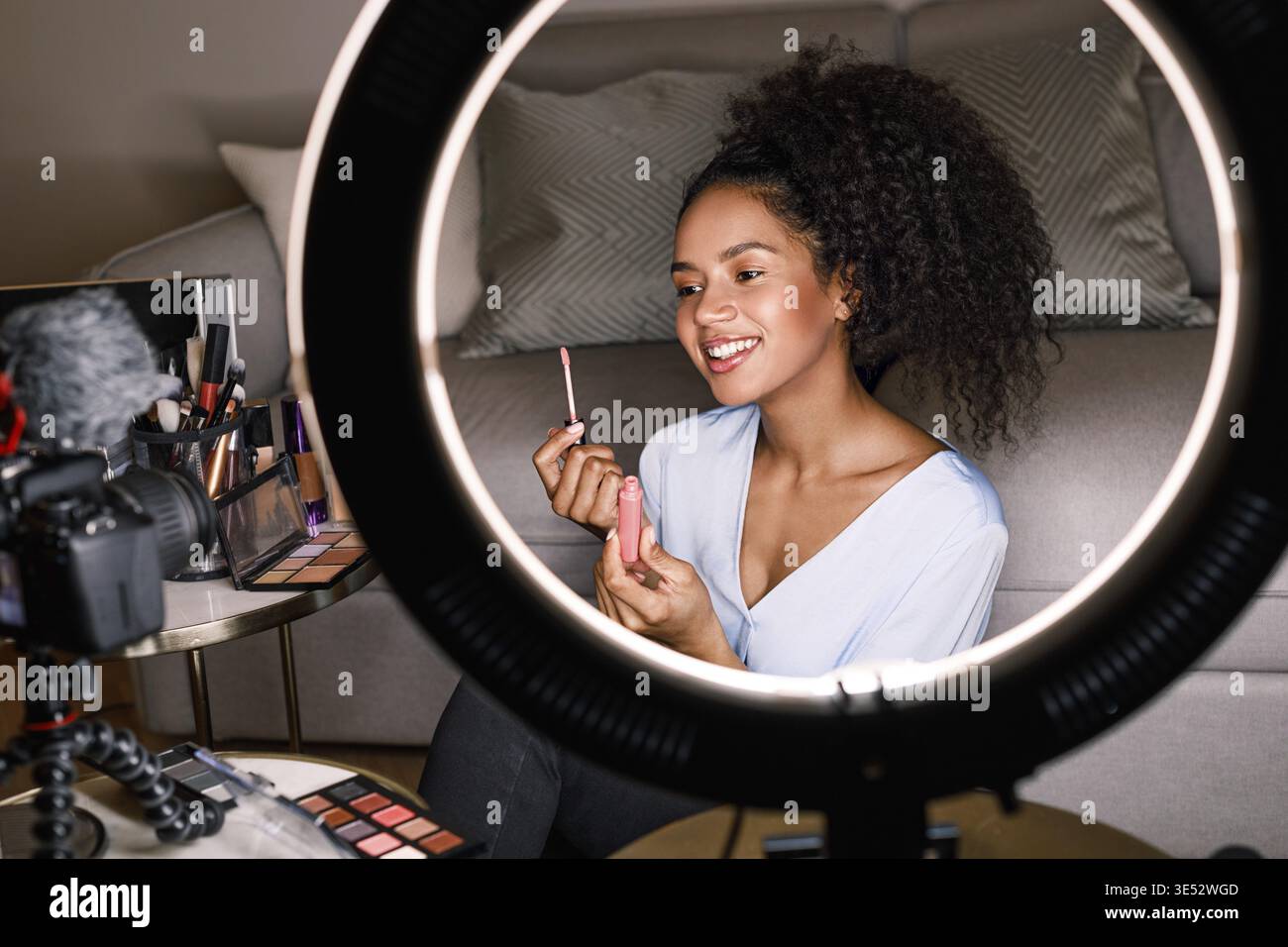 Smiling vlogger showing lipstick brush while recording a video Stock Photo