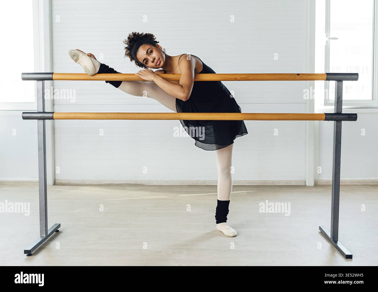 Young ballerina stretching her leg in dance studio. Woman doing exercise on ballet barre Stock Photo