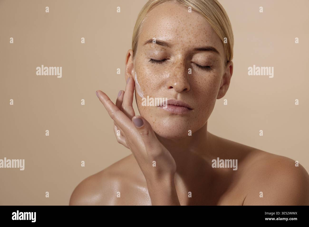 Beautiful female applying moisturizer on face in studio Stock Photo