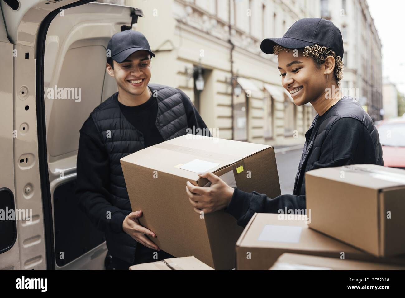 Two smiling couriers unloading cardboard boxes from van in the city Stock Photo
