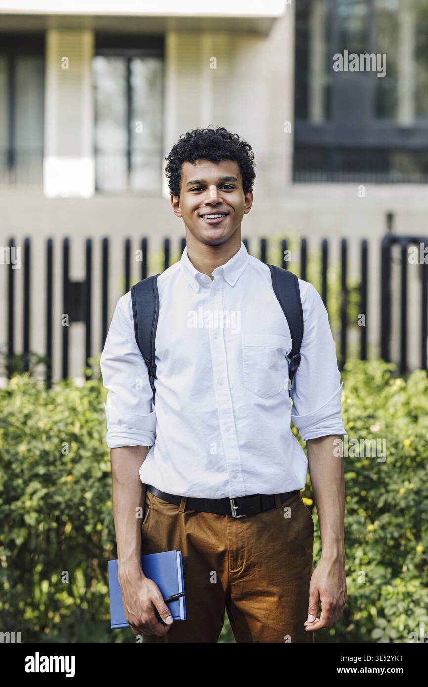 Handsome young man going standing outdoors with backpack and notebook Stock Photo