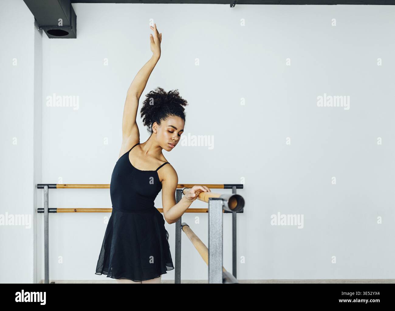 Young beautiful ballerina practicing ballet moves at barre in small studio Stock Photo
