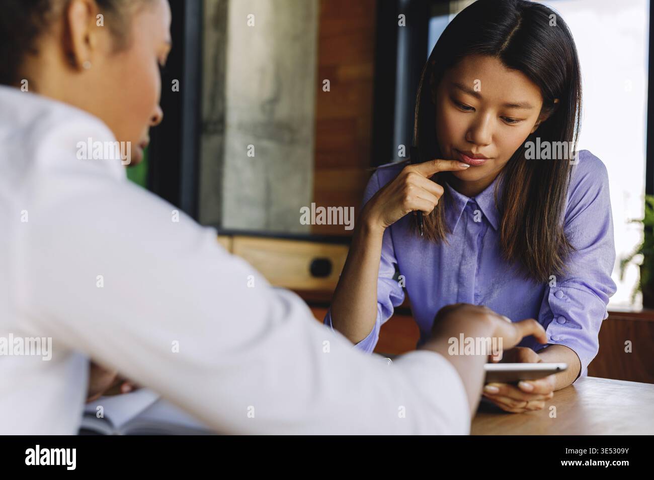 Two colleagues discussing new project, using digital tablet while sitting at table Stock Photo