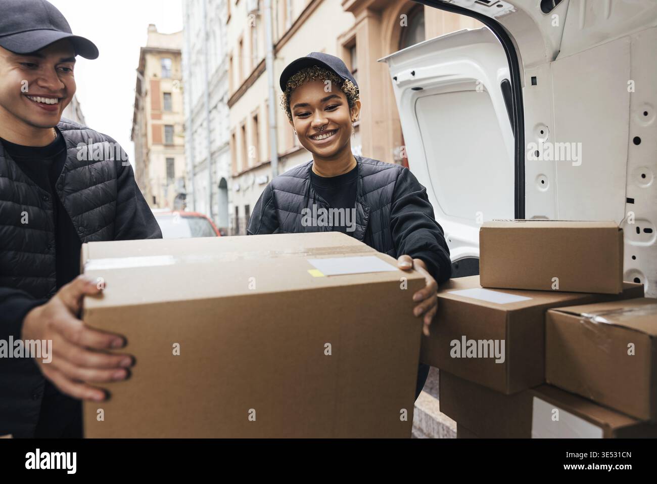 Two smiling coworkers unloading cardboard boxes from van for delivery Stock Photo