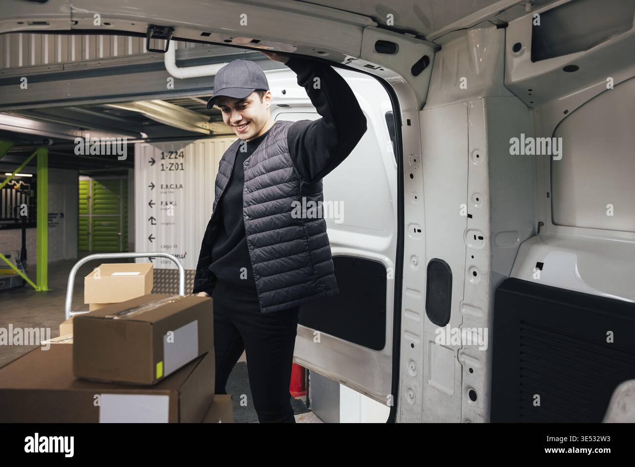 Confident courier leaning on van looking on cardboard boxes Stock Photo