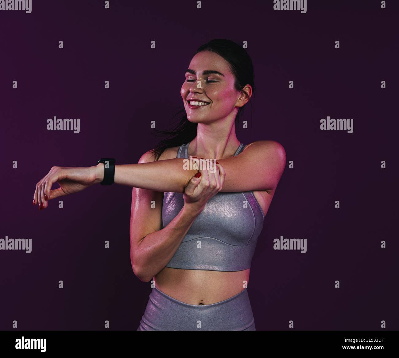 Young smiling female with closed eyes stretching and flexing her hands over magenta background in studio Stock Photo