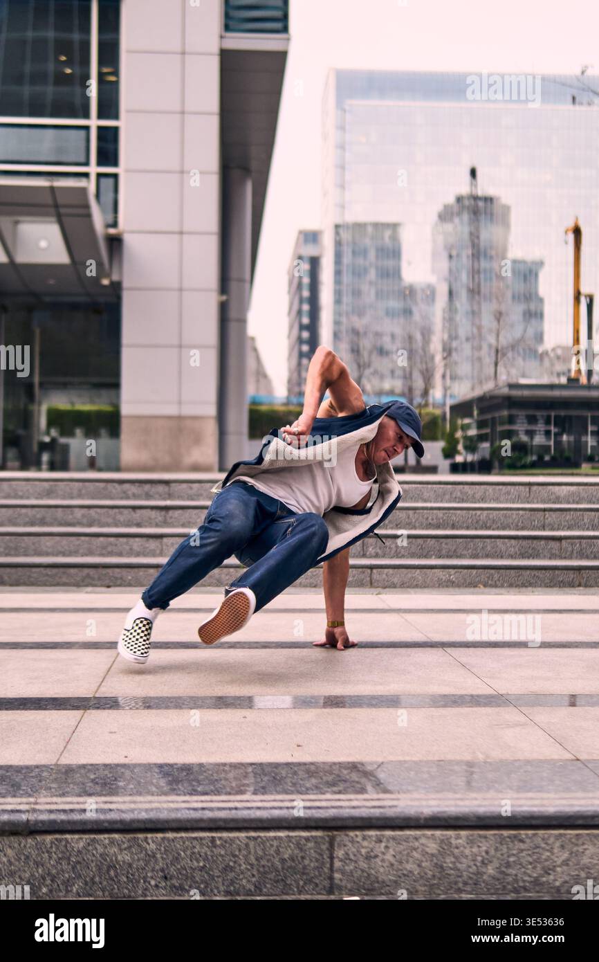Young adult enthusiastically break dancing in front of buildings, spinning Stock Photo