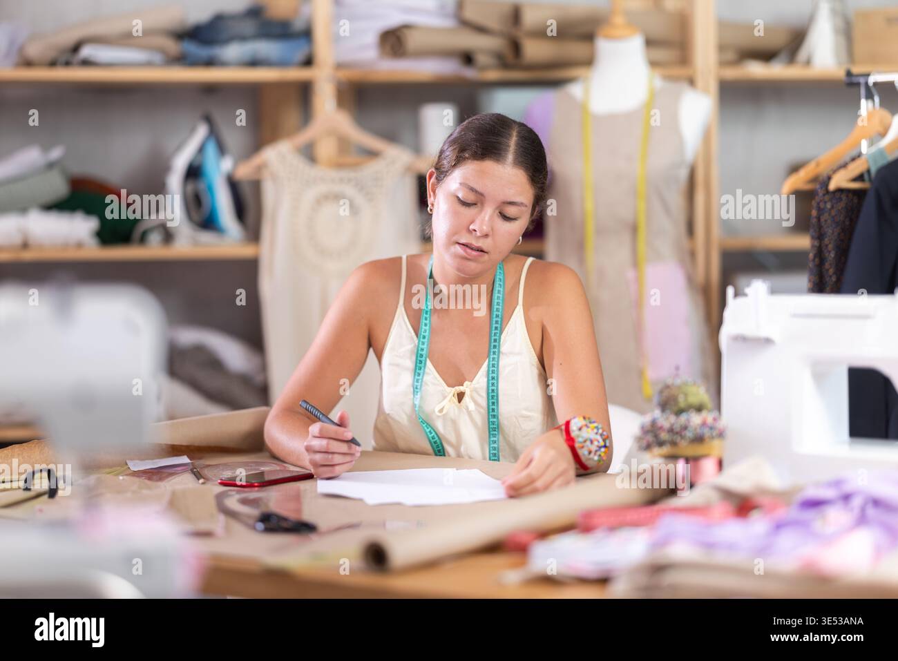 Young tailoress engaged in paperwork in sewing workshop Stock Photo