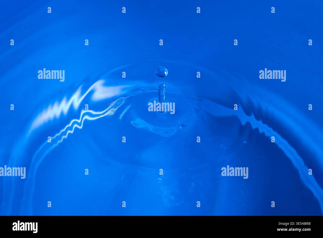 A drop of water falls and bounces on a wet surface against a blue background Stock Photo