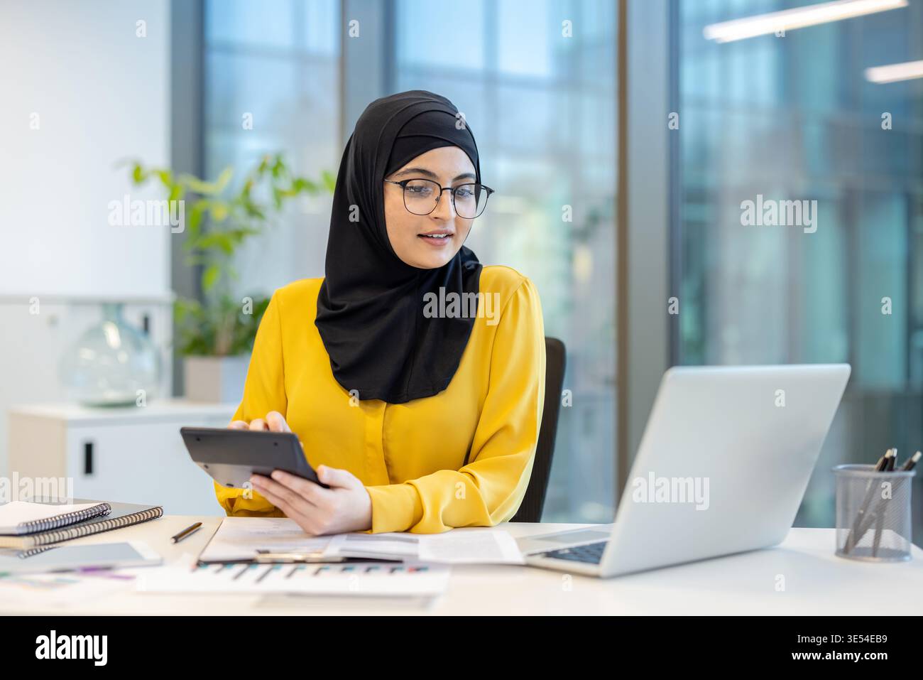 Muslim woman wearing a hijab and glasses, working on financial ...