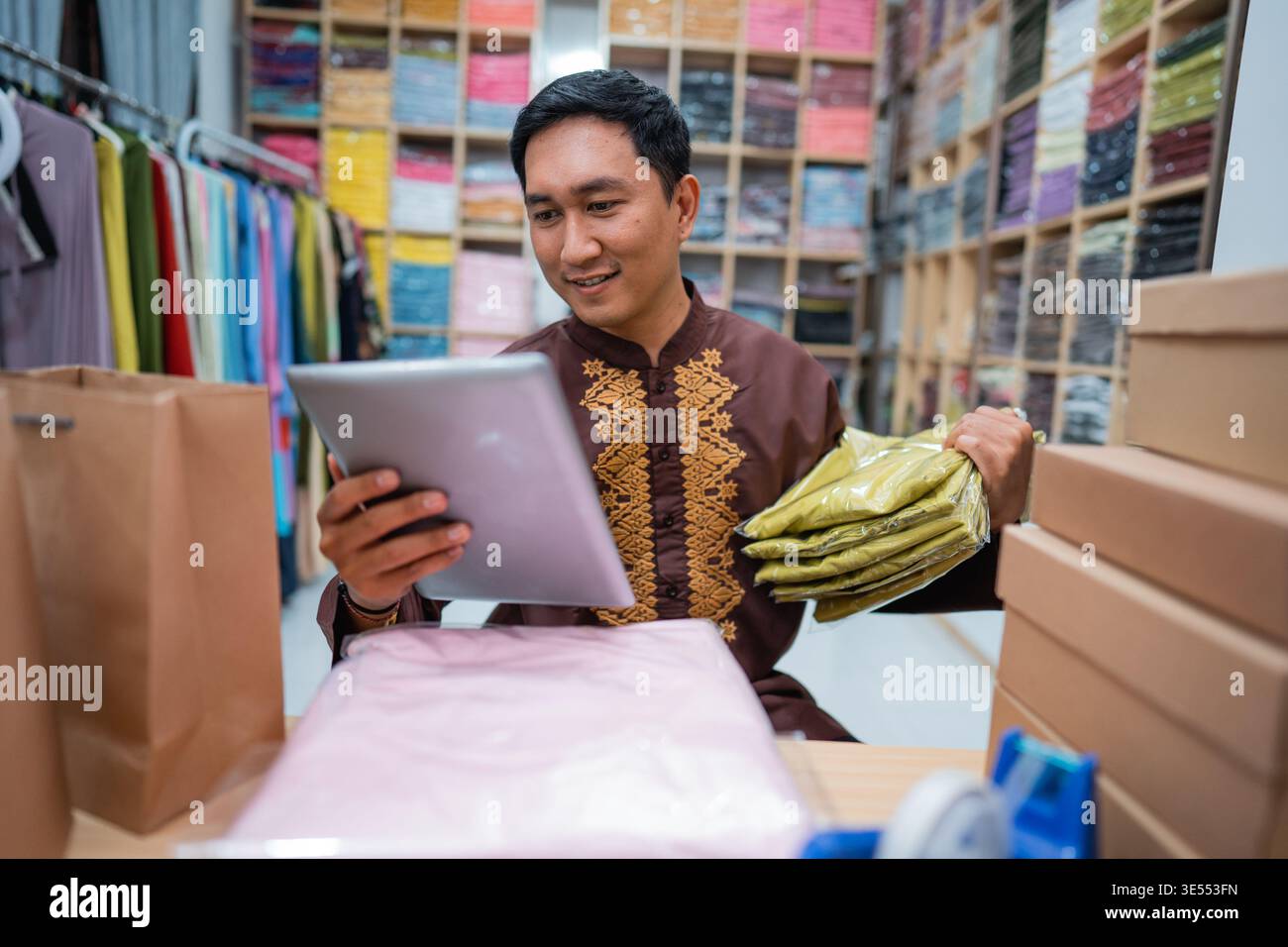 seller using tablet while sitting on a desk with his product Stock Photo