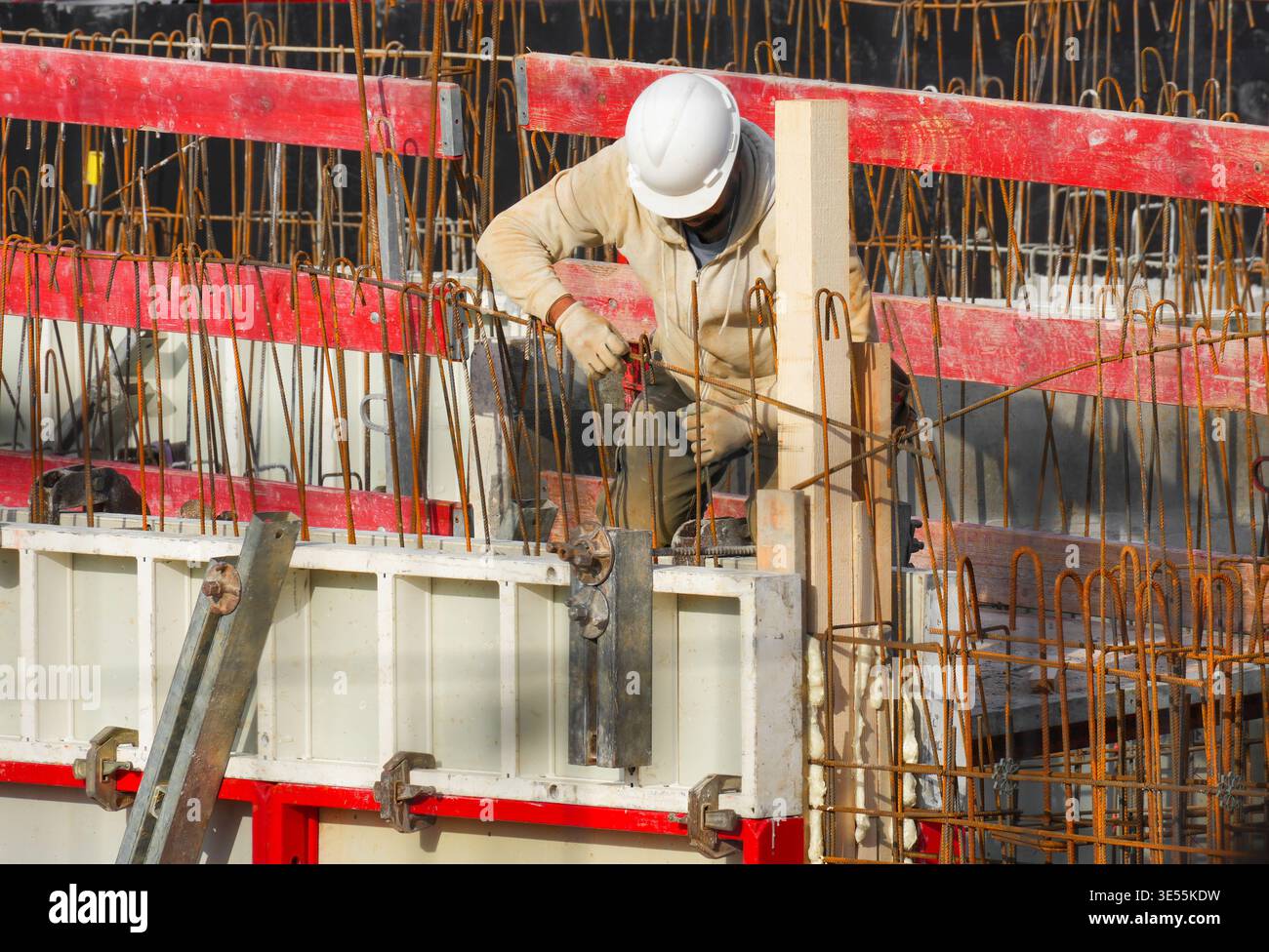 A constructor working with tools on building site with red wooden formwork, showing a heavy working process. Stock Photo