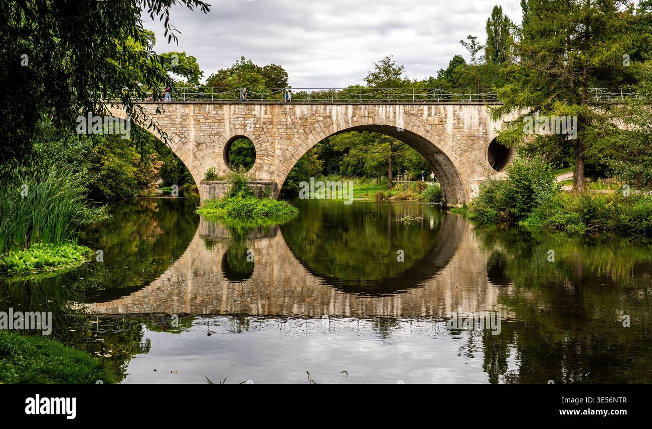 Stone arch bridge over calm river with mirror reflection, surrounded by ...