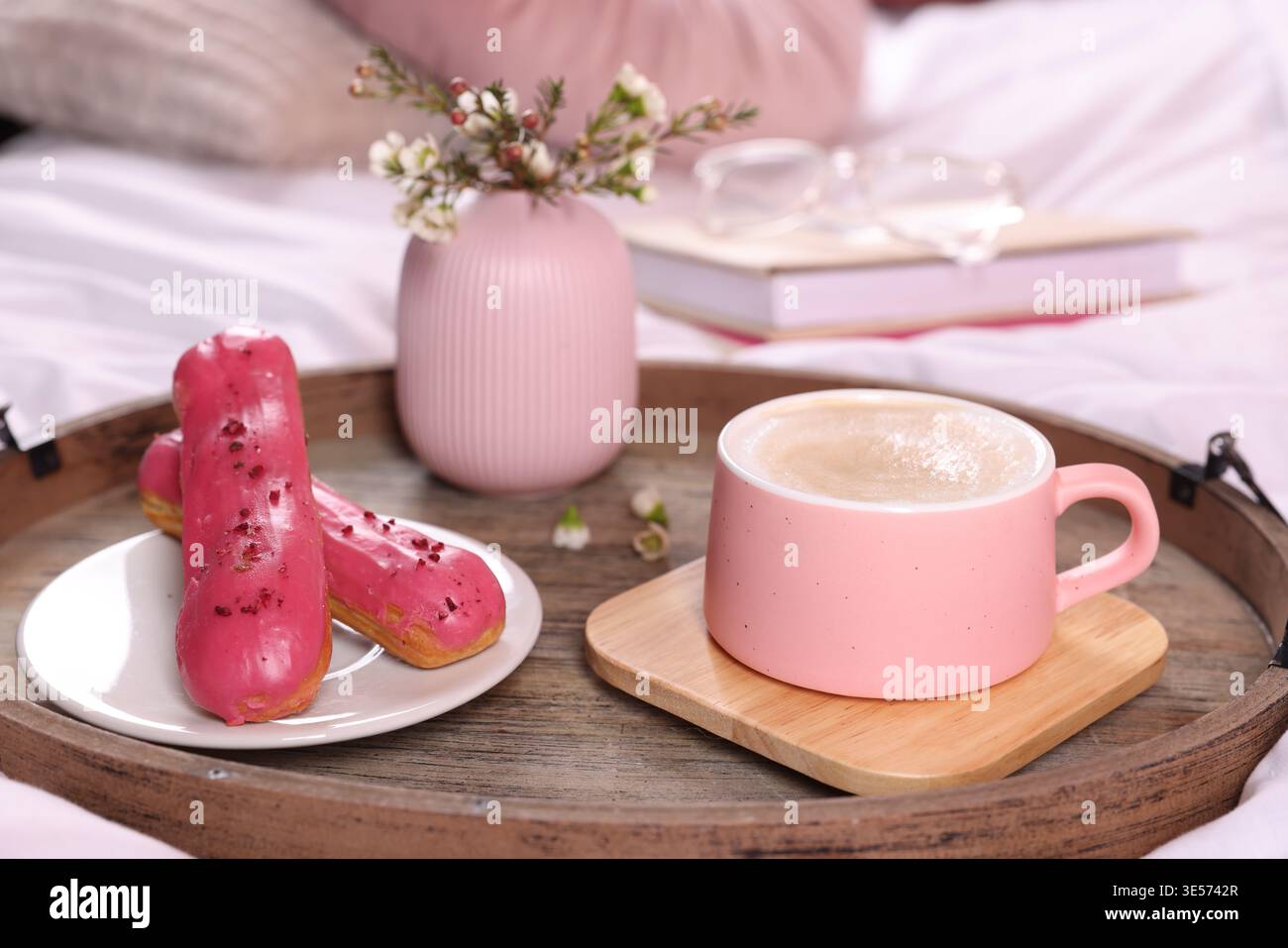 Aromatic coffee in cup, eclairs, and beautiful flowers on bed, closeup Stock Photo