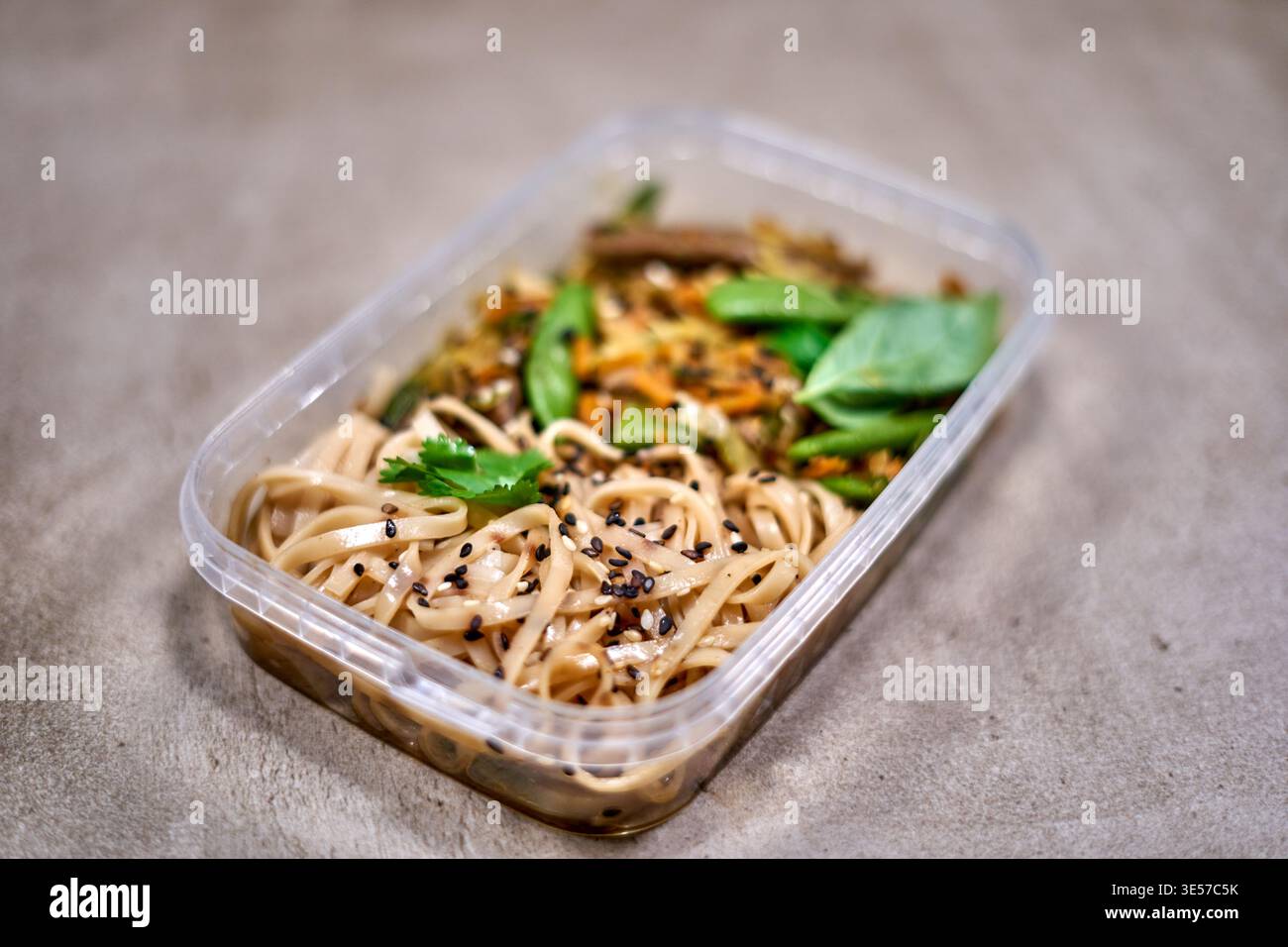 A close-up photograph of a rectangular transparent plastic meal prep container placed on a gray concrete or stone surface. The container holds an Stock Photo