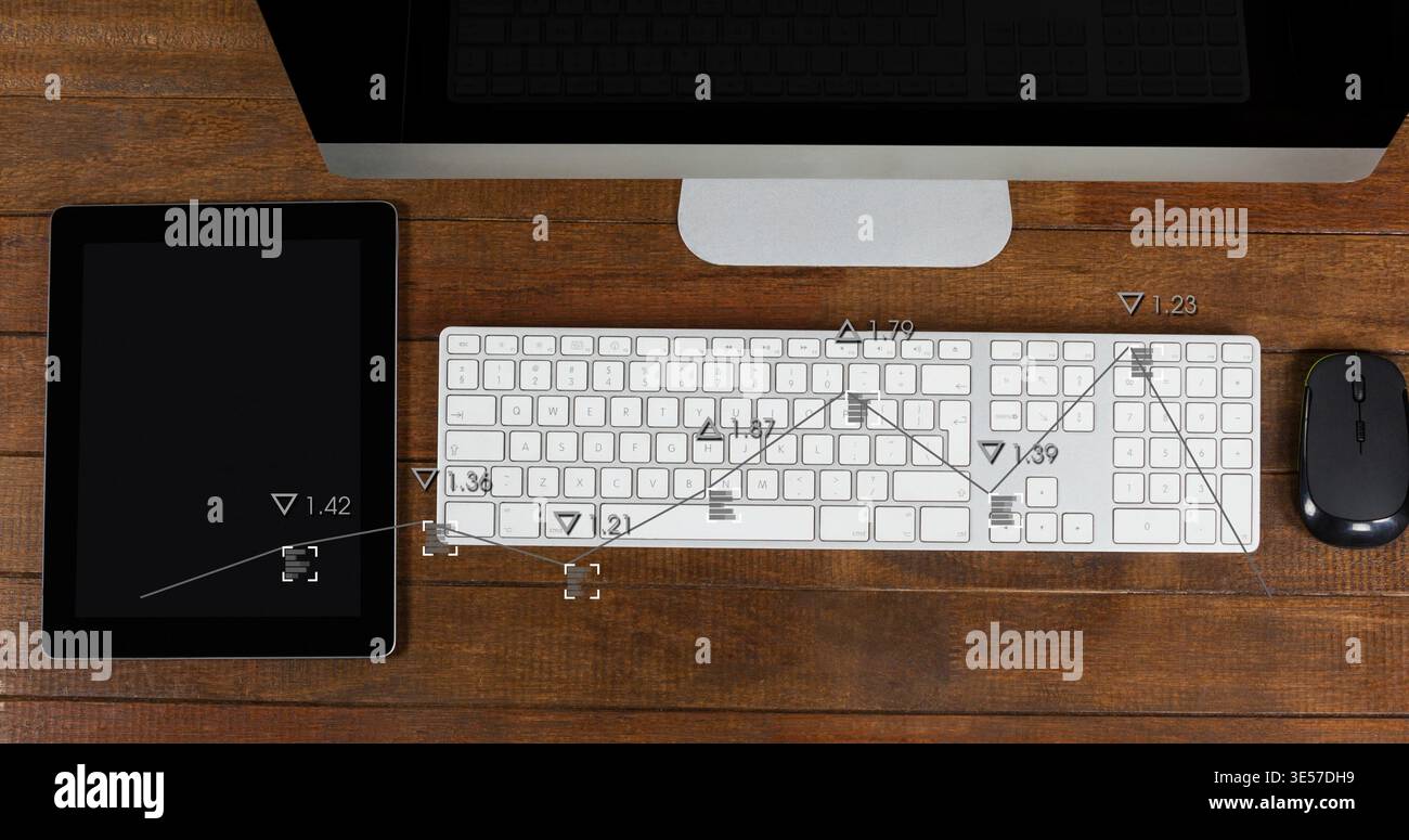 Displaying white computer keyboard centered on wood desk with monitor, tablet, mouse, data overlays Stock Photo