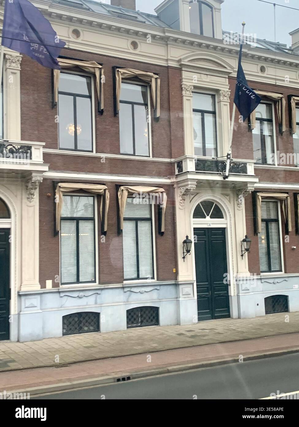 Historic European style townhouse with decorative facade and coloured flags displayed on the upper floors overlooking a tram lined street in Hague - Smartphone Captured Stock Image