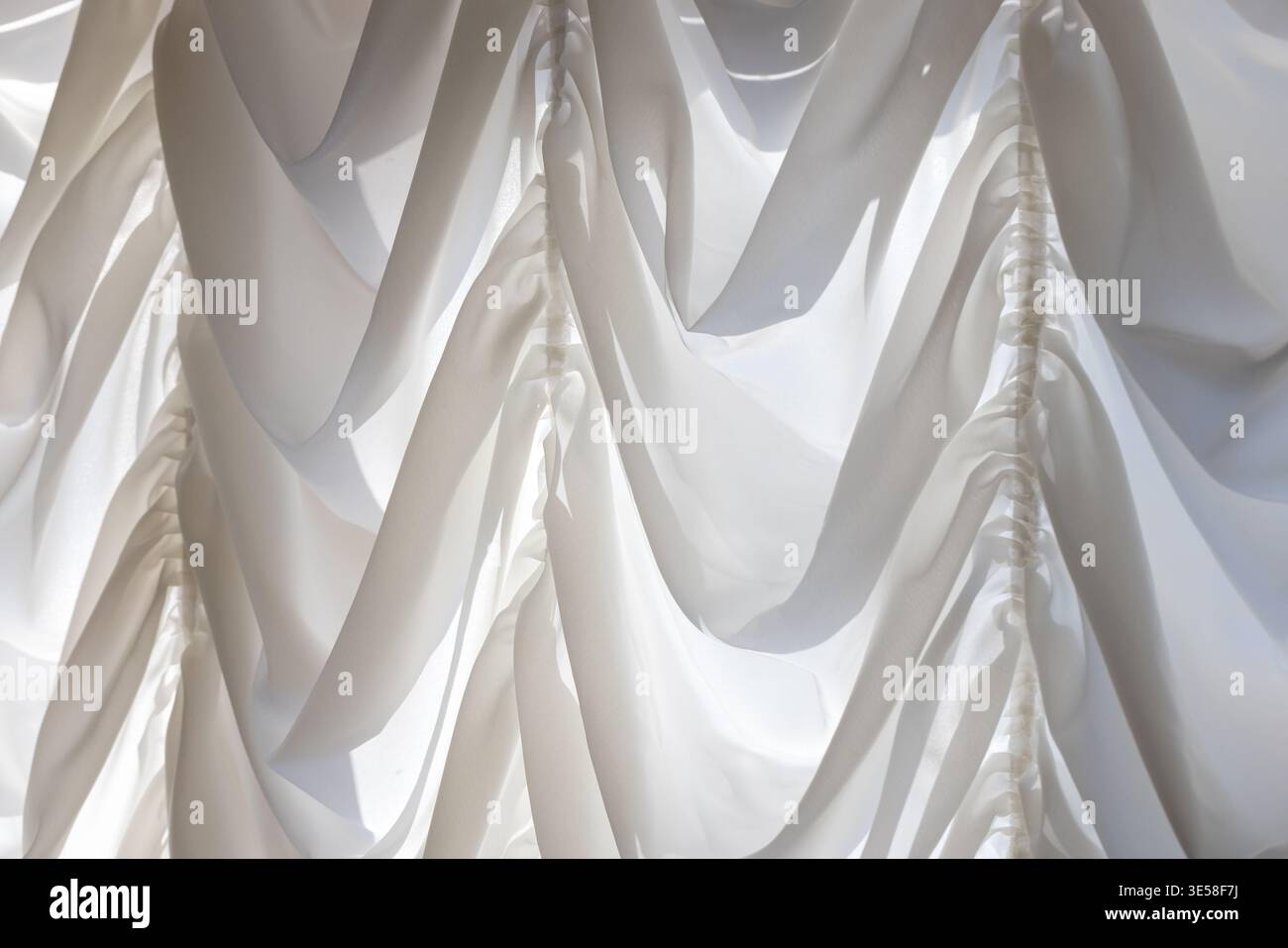 Soft white drapery with flowing pleats and ruched detailing creates an ...