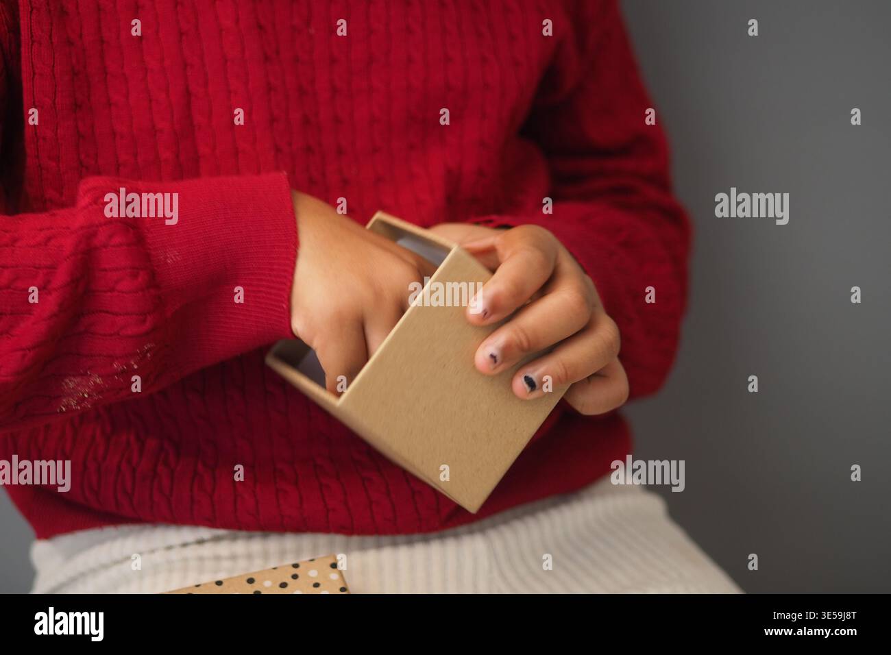 Child opens small box with hands in indoor setting Stock Photo