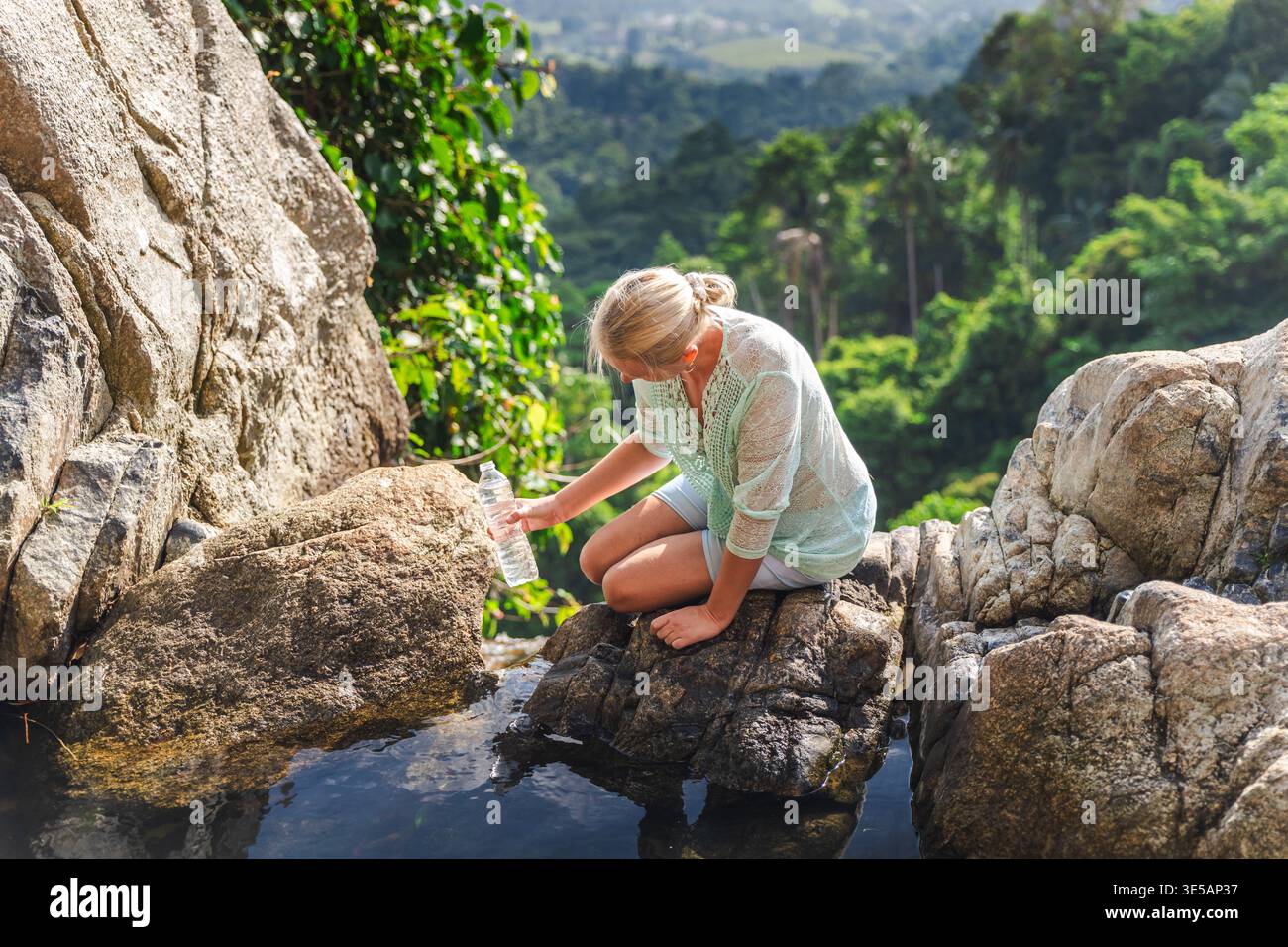 Woman collecting water from natural rock pool in tropical jungle ...