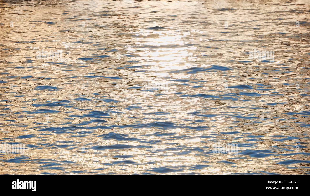 Golden hour light reflecting on rippling water surface creating sparkling texture Stock Photo